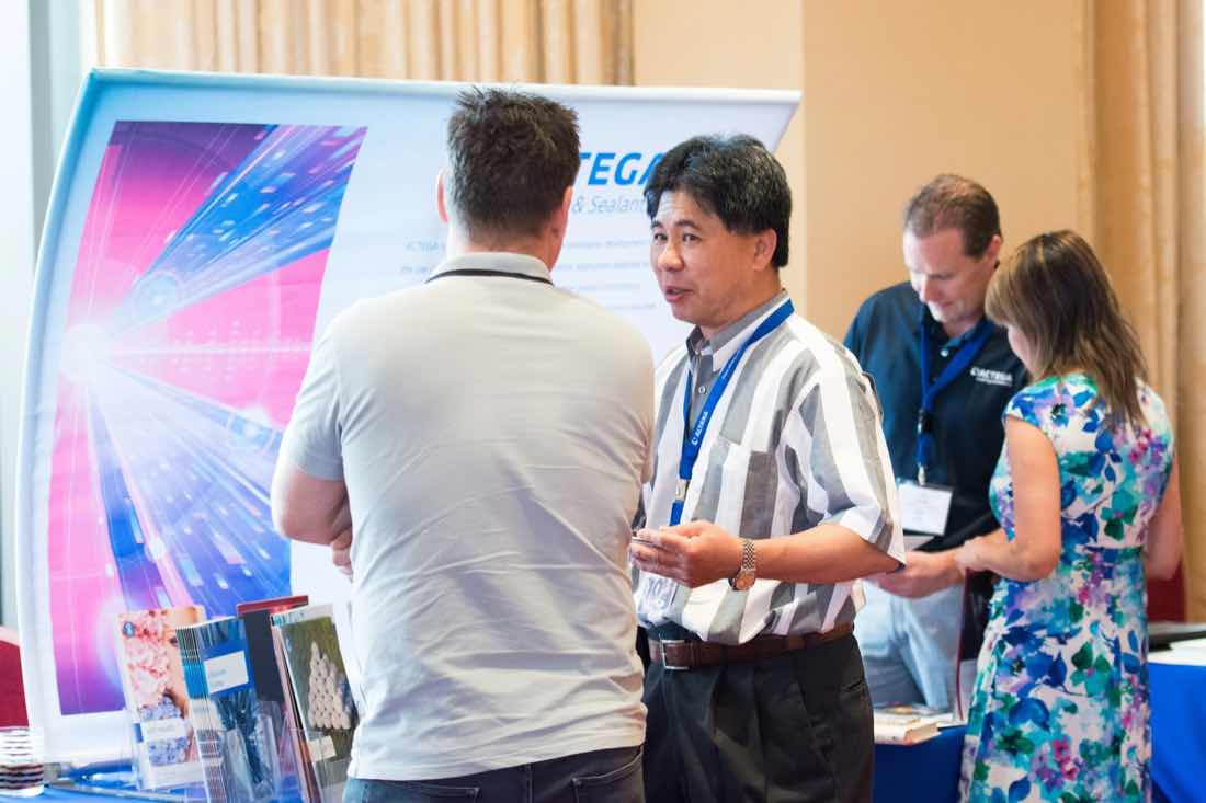 Attendees talking at a sponsor booth with a bright printed backdrop