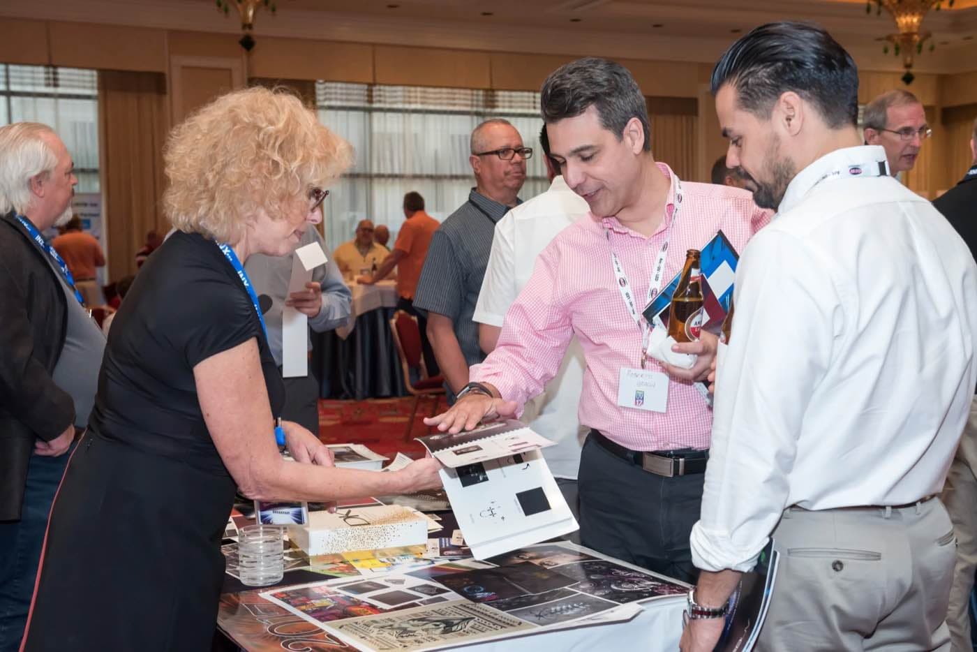 Attendee presenting a portfolio of printed pieces to two colleagues at a table
