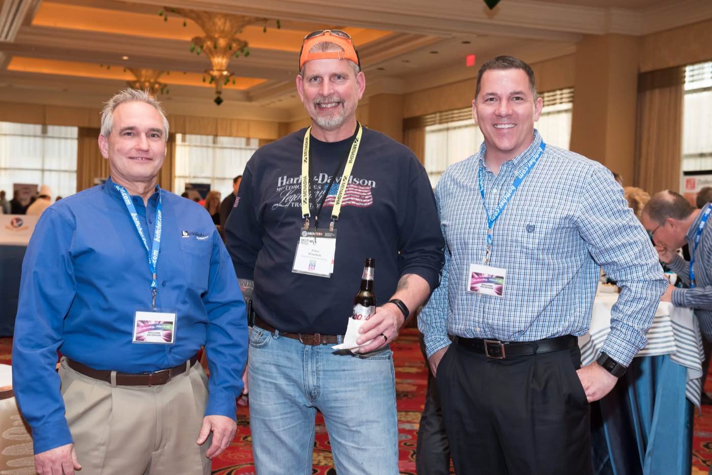 Three smiling attendees with drinks posing together at an evening reception