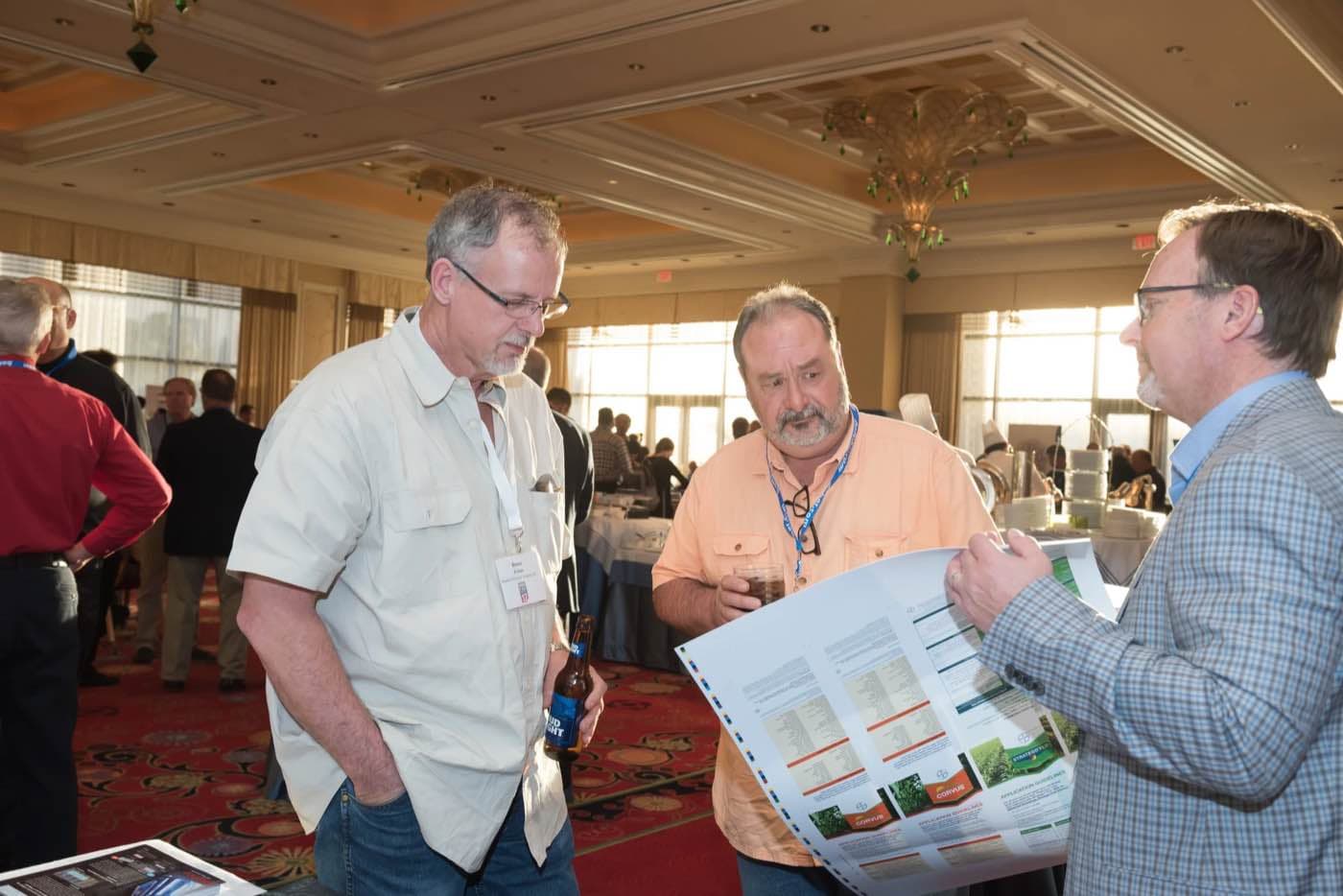 Three attendees examining a printed sample sheet together at the conference