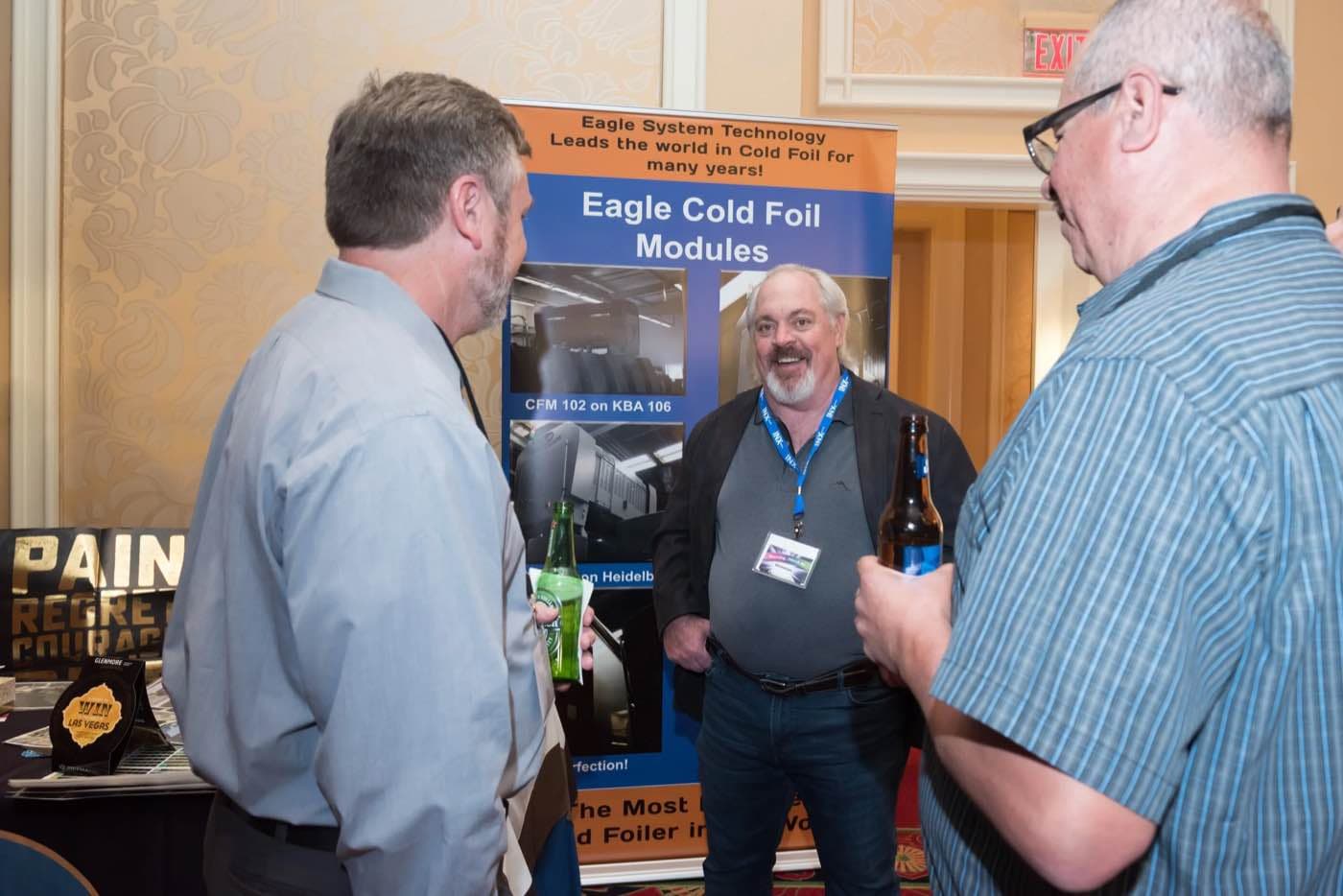 Attendees in conversation at a sponsor booth with a cold foil equipment banner