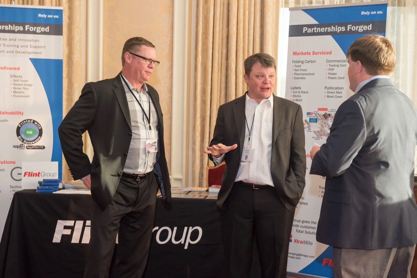 Three men in conversation at a sponsor booth with partnership banners