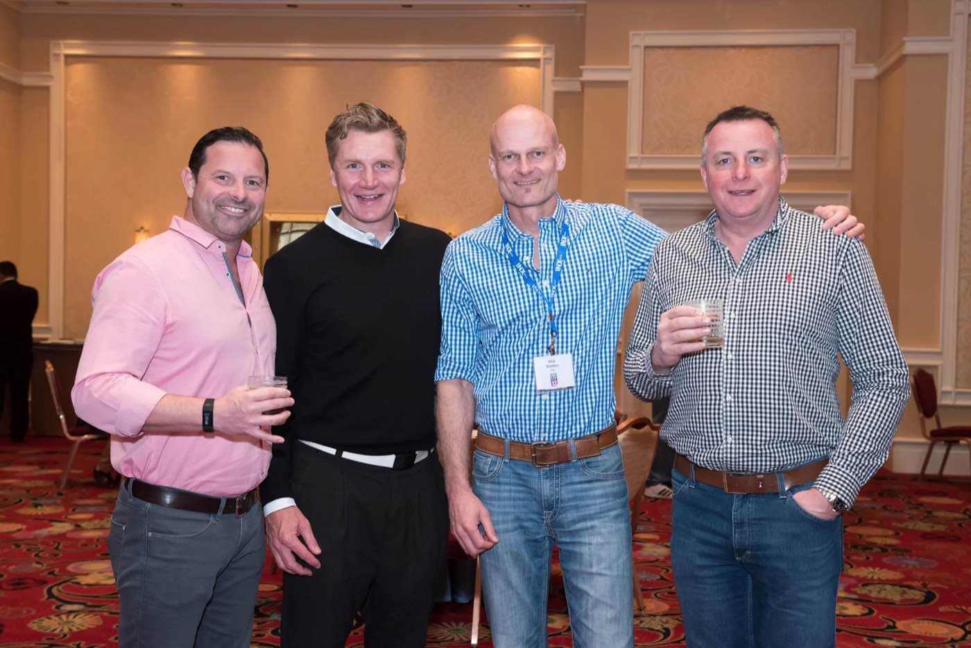 Four attendees with drinks standing together at an evening networking event