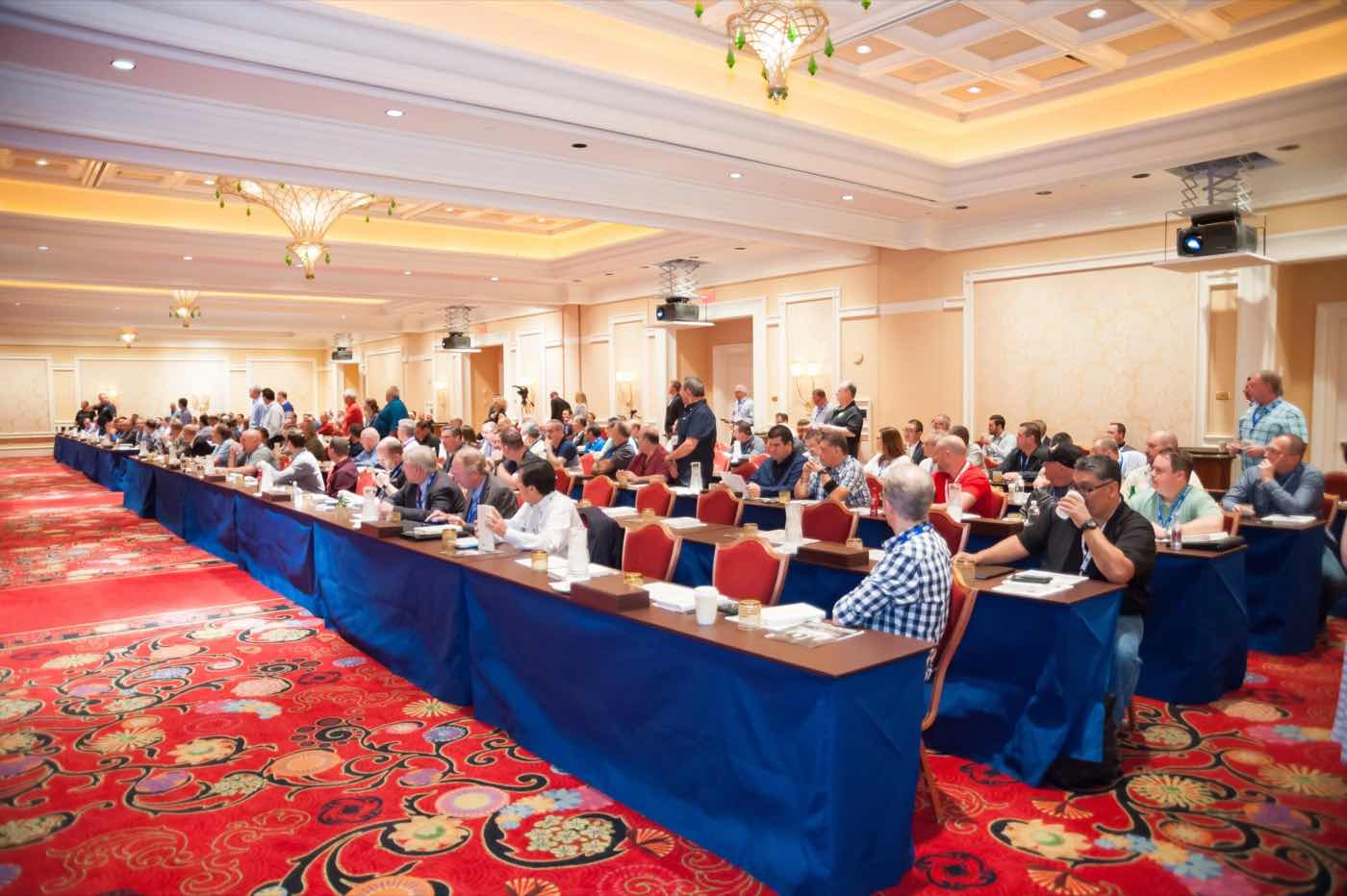 Wide view of a full conference ballroom with attendees seated at long classroom tables