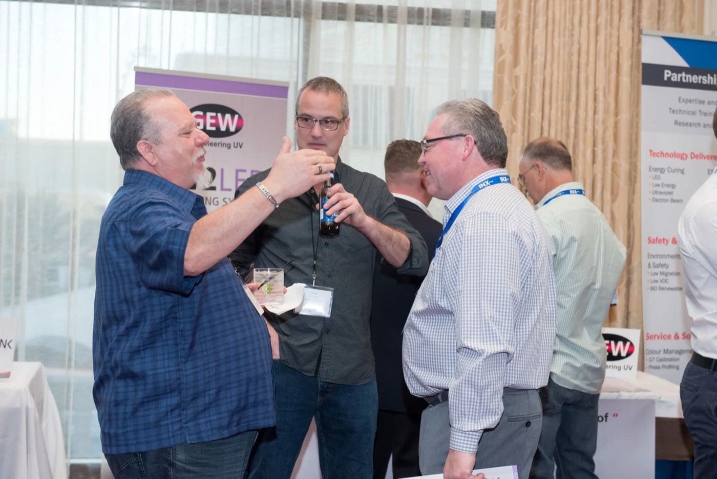 Group of attendees with drinks talking beside a UV-curing sponsor booth