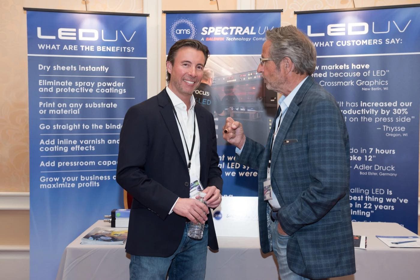 Two attendees talking in front of sponsor banners describing LED UV benefits