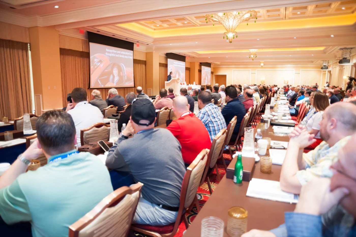 Conference audience seen from the back of the room facing two projection screens