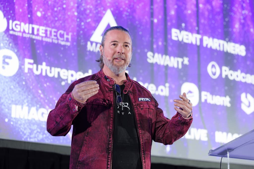 Steve Metcalf speaking on stage against a purple starfield backdrop at an Imagine AI Live keynote